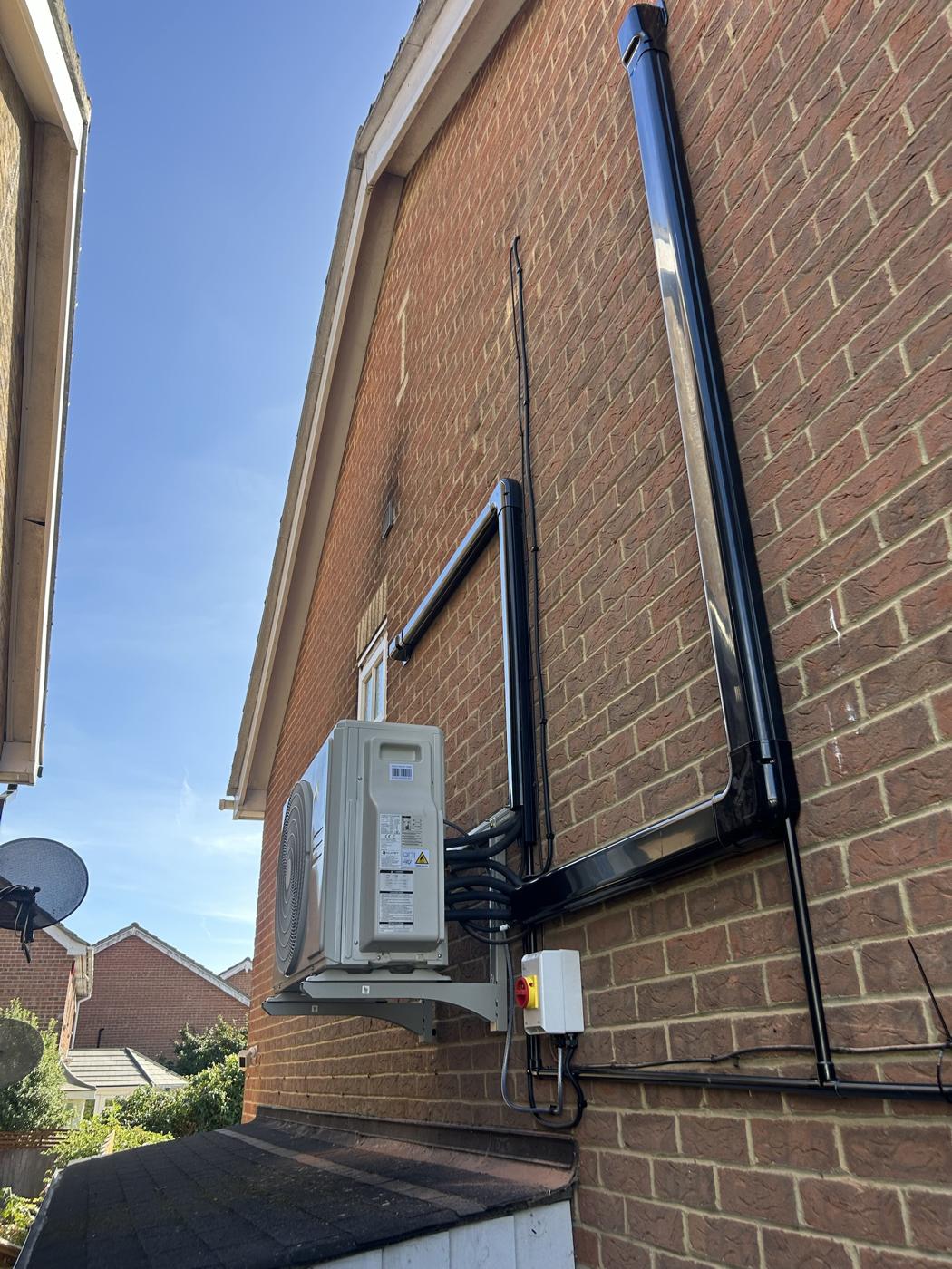 Outdoor unit on wall brackets with black trunking on brickwork
