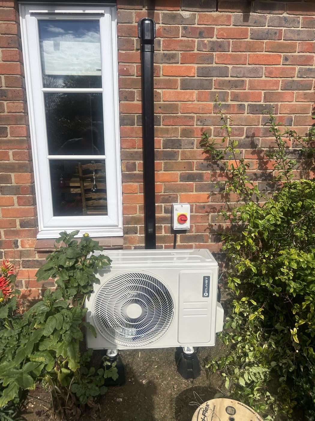 Outdoor unit at ground level beside a garden window with isolator