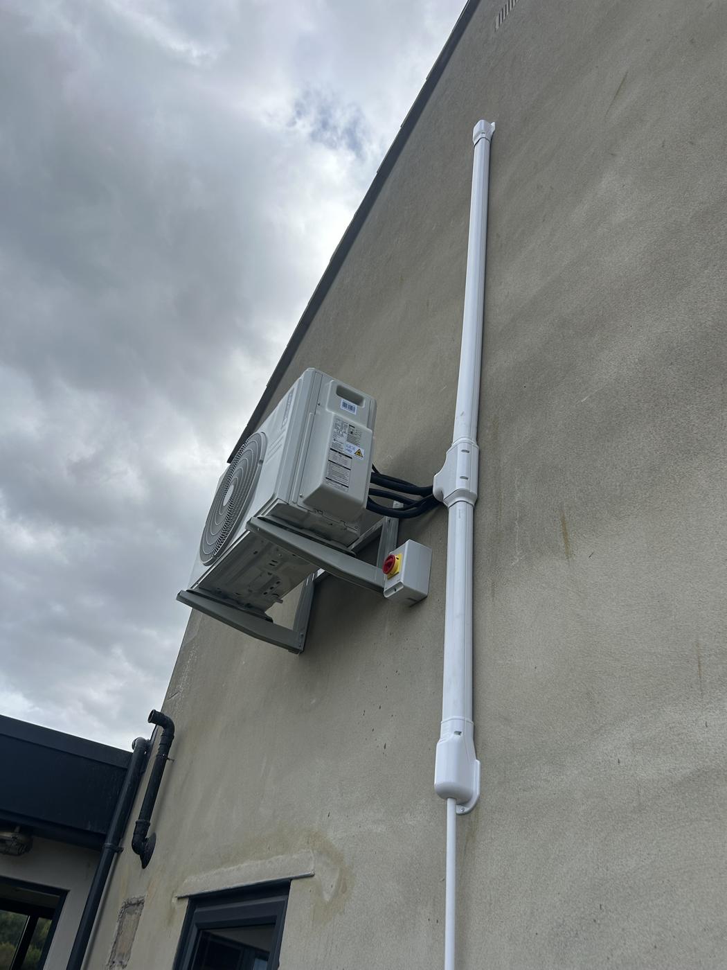 Outdoor unit on a rendered wall with white trunking to first floor